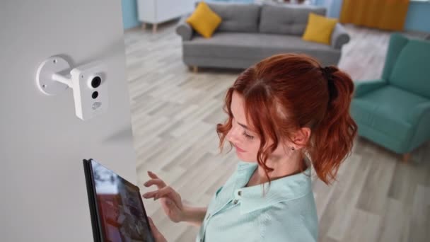 Femme propriétaire contrôle la vidéosurveillance à domicile avec tablette à l'intérieur, fille vérifiant la caméra avec gadget dans ses mains — Video