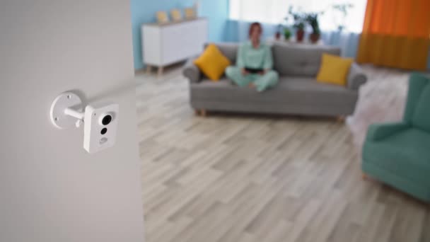 Caméra de surveillance moderne sur le mur dans un appartement confortable, femme avec tablette PC assis sur un canapé en arrière-plan — Video