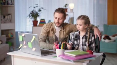 Baba, okulda öğrenim gören şirin kız çocuğuna yardım etmek için ev ödevlerini kontrol ediyor.