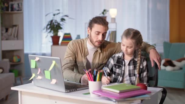 Homem carinhoso ajuda sua criança do sexo feminino a fazer lição de casa, enquanto a distância de ensino em casa devido à quarentena — Vídeo de Stock