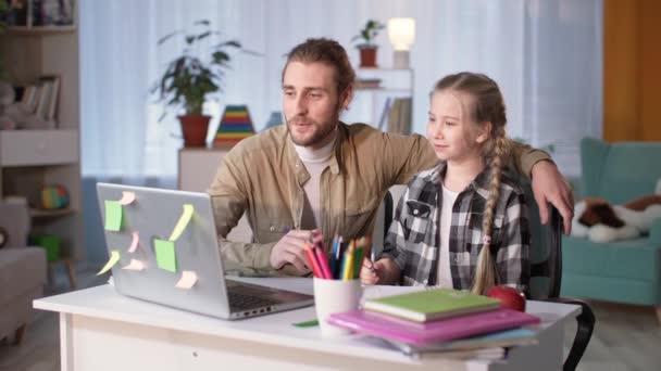 Padre o tutor explicando tareas que ayudan a las niñas en edad escolar con estudios durante la lección en línea en la mesa de la habitación — Vídeo de stock