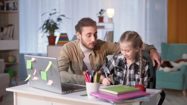 Homme aide fille à faire des devoirs pendant l'apprentissage à distance à la maison tout en étant assis dans la chambre à la table — Video