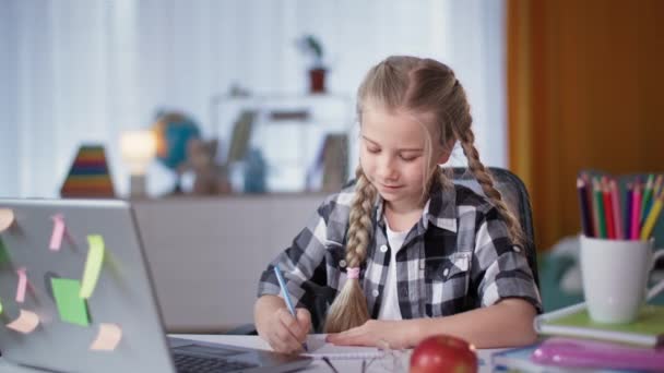 Девушка делает домашнее задание в комнате, сидя за столом с ноутбуком во время карантина — стоковое видео