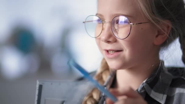メガネをかけた女子小学生は自宅で隔離中にコンピュータのビデオリンクを介して教師とオンラインレッスンを受ける — ストック動画