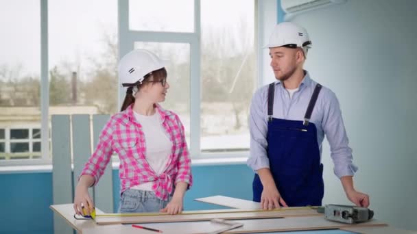 Man and woman in safety helmet repair indoor floor and cut laminate with construction tools — Stock Video