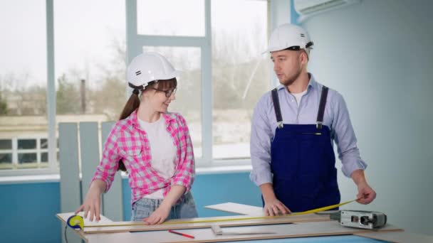 Homem e mulher em capacete de segurança reparando chão na sala e corte laminado com ferramentas de construção — Vídeo de Stock