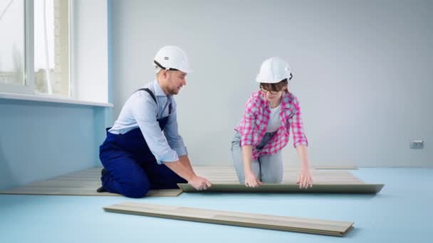 Equipe de homem e mulher que estabelece laminado, fechaduras de tricô e dando cinco uns aos outros enquanto renovando o chão em um apartamento — Vídeo de Stock