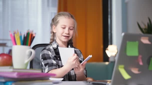 Female fish doing homework with teacher online using video communication on computer and showing cards on laptop screen while sitting at home at table in room — Stock Video