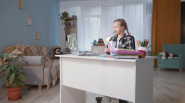 İlkokul öğrencisi video iletişimiyle öğretmenle ödev yapıyor ve masada oturan bilgisayar ekranında harflerle kartları gösteriyor.