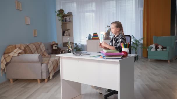 Mädchen ist mit Lehrerin per Videokommunikation am Computer am Tisch im Zimmer beschäftigt — Stockvideo