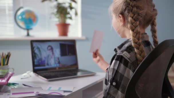 Menina está envolvida em aulas com o professor via vídeo no laptop e ensina lição de casa on-line sentado à mesa no quarto — Vídeo de Stock