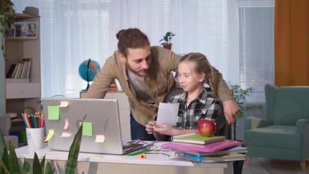 Otec pomáhá své dceři naučit se lekce on-line s učitelem přes video odkaz během karantény doma — Stock video