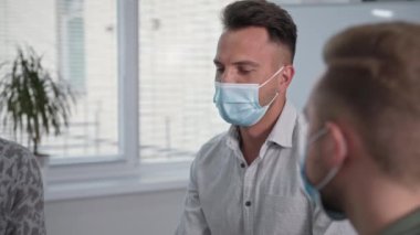 Virüs ve enfeksiyondan korunmak için tıbbi maske takan genç bir adamın portresi grup terapisinde güven çemberinde otururken deneyimlerden bahsediyor.
