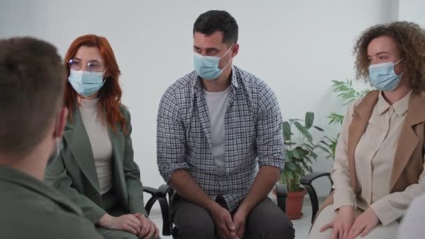 Обучение во время пандемии, молодая женщина в медицинской маске для защиты от вируса и инфекции делится психологическим и эмоциональным опытом во время групповой терапии в кругу доверия — стоковое видео