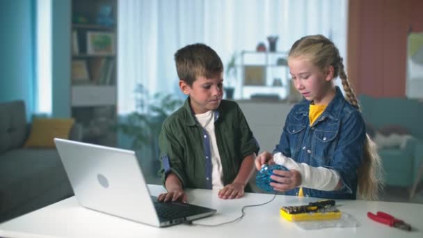 Programação de computador de tecnologia por crianças, menino e menina com gesso no braço conectado o drone via cabo USB para o laptop em casa — Vídeo de Stock