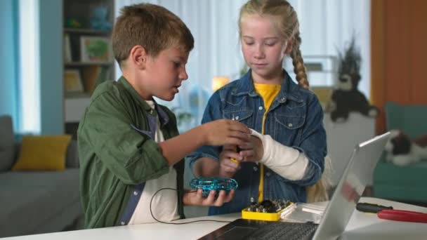 Chico inteligente con una herramienta y una chica con yeso en la mano están estudiando el trabajo de quadrocopter, los niños están utilizando un ordenador portátil en casa — Vídeos de Stock