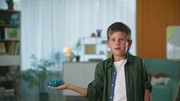 Brinquedos interativos, pequeno drone pairando sobre a mão de um menino pequeno voa para longe, criança masculina aponta dedo para o lado dentro de casa — Vídeo de Stock
