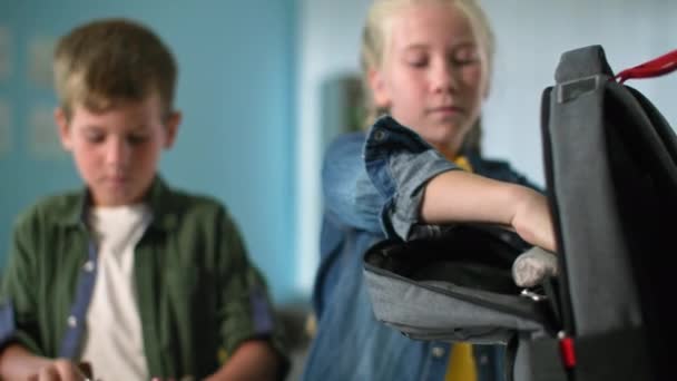 Eğitim, okul çantalarını okul malzemeleriyle dolduran çocuklar, alçılı kız ve oğlan evde başparmaklarını gösteriyorlar. — Stok video