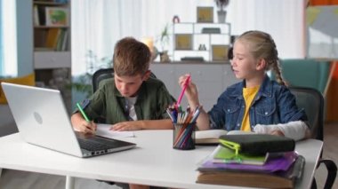 Evde eğitim gören, bilgisayar laptopuyla masada otururken kolunda alçı olan kız kardeşiyle internetten ders çalışan tatlı bir çocuk.