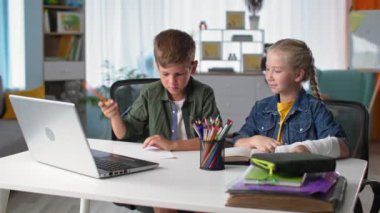 Çocuklar internetten öğreniyor. Kolunda alçı olan bir kızla çalışan tatlı bir çocuk. Evde bilgisayar laptopuyla oturuyor.