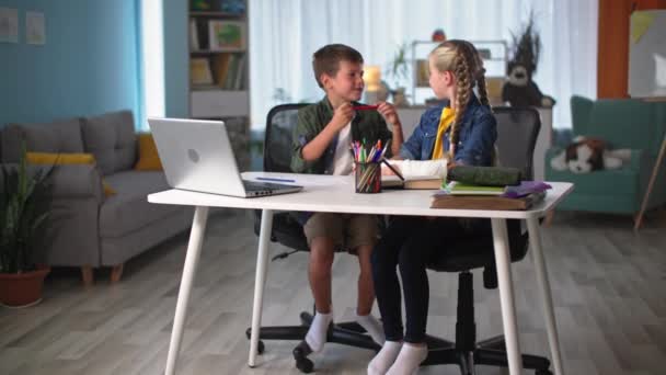 Счастливого детства, мальчик и девочка с гипсовым гипсом на руке рисуют, сидя за столом во время домашнего обучения, а затем дурачиться с цветными карандашами — стоковое видео