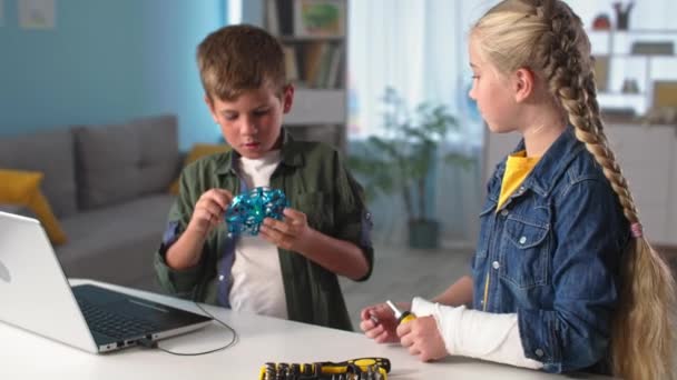Crianças inteligentes, irmão com ferramentas e irmã com gesso fundido em seu braço conectado mini quadricóptero para laptop em casa — Vídeo de Stock