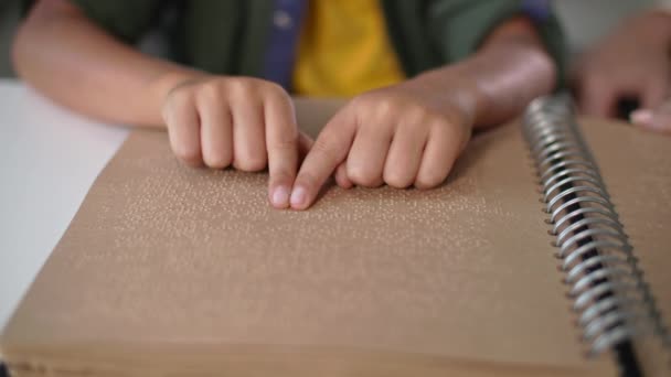 Kinderhände lesen Braillebuch mit Schriftzeichen für Sehbehinderte aus nächster Nähe, Mutter sitzt in der Nähe und hilft blindem Sohn am Tisch drinnen — Stockvideo