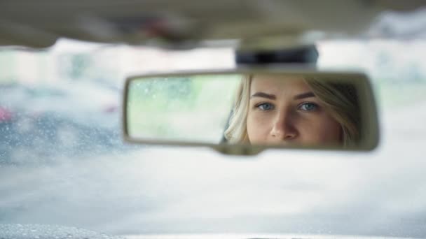 Conductor femenino sonriente sentado mirando en el espejo retrovisor mientras está sentado en un coche, de cerca — Vídeos de Stock