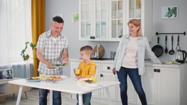 Almuerzo familiar, padres alegres de cuidado junto con su hijo pequeño mesa para la cena conjunta en el fondo de la cocina — Vídeo de stock