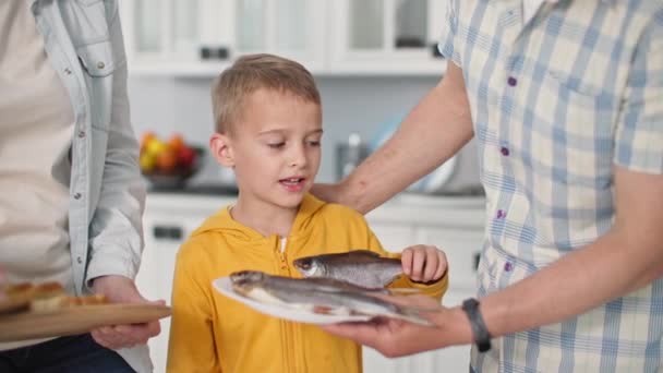 Portré a kis aranyos férfi gyermek szedés tenger csótány étkezés tányér a szülők otthon háttér konyha — Stock videók