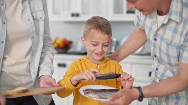 Fruits de mer, joyeux petit garçon choisit le poisson pour collation avec maman et papa à la maison sur fond de cuisine — Video