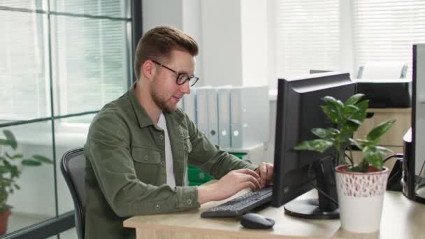 Ung kontorsarbetare bär manliga glasögon arbetar vid datorn bakgrund fönster — Stockvideo