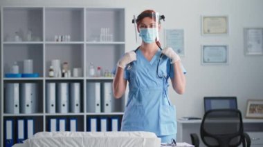 Tıbbi maske takan ve koruyucu kalkan takan kadın veteriner portresi. Doktorun ofisinde kameraya bakarken güvenli bir şekilde kollarını kavuşturmuş.