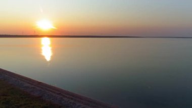 Kamyonların ve arabaların hava görüntüsü, araçlar gün batımında deniz kenarında yol boyunca ilerliyorlar.