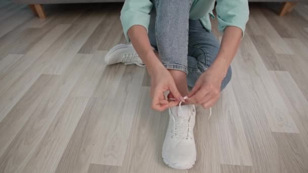 Mujer joven sentada en el suelo ata sus cordones en zapatos deportivos cómodos para caminar con amigos en el parque, primer plano — Vídeo de stock