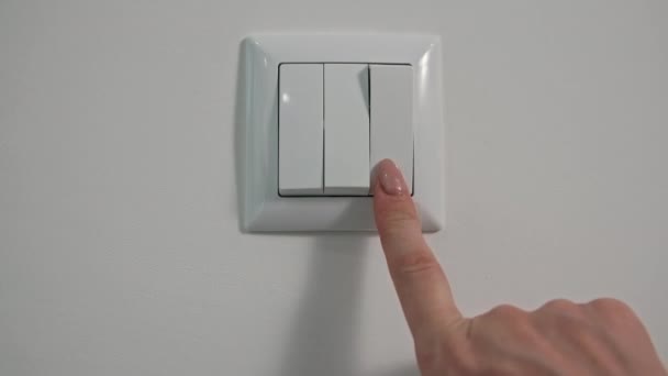 Las mujeres jóvenes apagan las luces en las habitaciones con interruptor en la pared blanca, primer plano — Vídeos de Stock