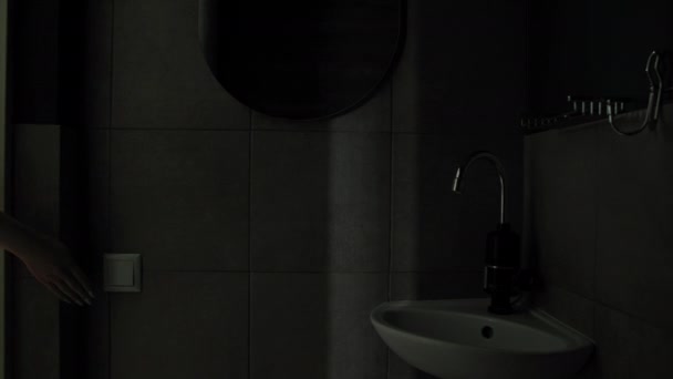 Mujer joven enciende la iluminación con interruptor en el baño, energía eléctrica — Vídeos de Stock