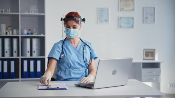 Онлайновая консультация врача, женщина-ветеринар в медицинской маске на лице общается по видеосвязи с пациентом, сидящим в больничном кабинете — стоковое видео