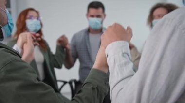 İş toplantısı, tıbbi maske takan kadın ve erkeklerden oluşan bir ekip kollarını kaldırıp indirdikten sonra terapi seansı sırasında çember halinde otururken birbirlerini alkışlıyorlar.