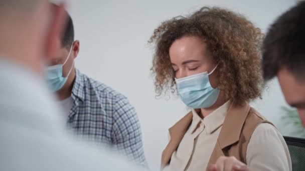 Portret van jonge vrouw in medisch masker houdt handen van mannen aan zij tijdens collectief gebed in therapie sessie — Stockvideo