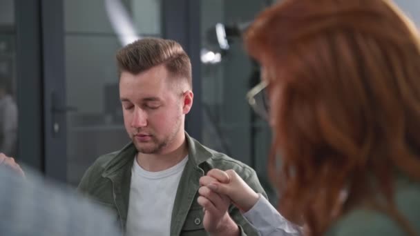 Portrait of a young man holding the hands of friends and with closed eyes prays to God during a group therapy session — стоковое видео