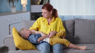 Mutlu erkek çocuk annesiyle oynarken eğleniyor, sevgi dolu kadın ebeveyn oğluyla arkadaşlık ediyor ve onu kanepede otururken gıdıklıyor.