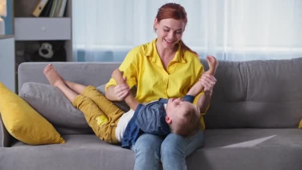Kapcsolat gyerekekkel, szerető nő szórakozás kis nevető fiú a kanapén, miközben pihenni otthon együtt — Stock videók