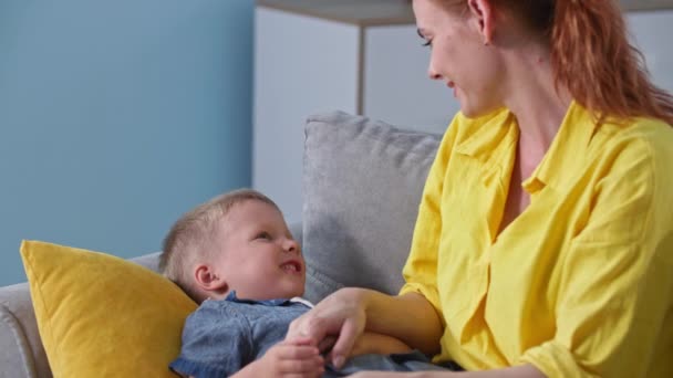 Mosolygós fiatal szülő csiklandozza a kisfiát szeretettel a családi nyaralás alatt otthon — Stock videók