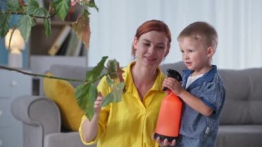 Ebeveynlere yardım eden küçük bir erkek çocuk, elinde bir spreyle annesine katılıyor. Aile tatilinde yeşil bir bitkiyi suluyor.