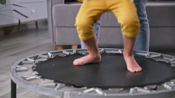 Juegos activos, piernas de un niño saltando alegremente en un trampolín junto a mamá en la habitación, primer plano — Vídeos de Stock