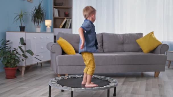 Vidám kis hím gyermek szórakoztató játszani és ugrál trambulinon a nappaliban otthon — Stock videók