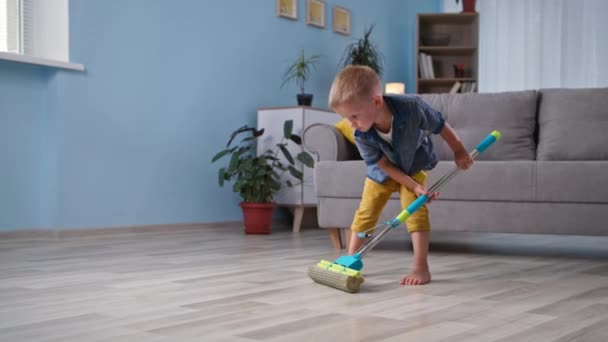 Ajudando os pais, bonito menino ajuda os pais a limpar a casa e esfrega o chão na sala — Vídeo de Stock