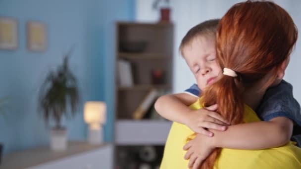 Ibu, seorang ibu yang peduli menikmati memeluk anaknya laki-laki dalam pelukannya dan membelai dia di belakang, anak laki-laki kecil melihat kamera — Stok Video