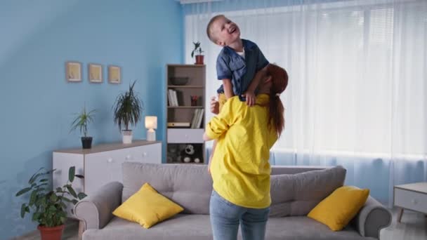 Gyermekkor, olvasható mosolygós férfi gyermek szórakozik az anyák karjai alatt családi nyaralás otthon — Stock videók